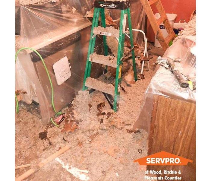 A devastated kitchen with debris covering everything and a ladder in the middle, covered in saw dust