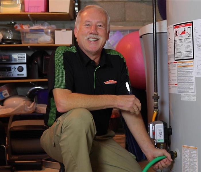 Co-owner, Steve Seckman, kneeling beside a hot water tank smiling and holding a hose